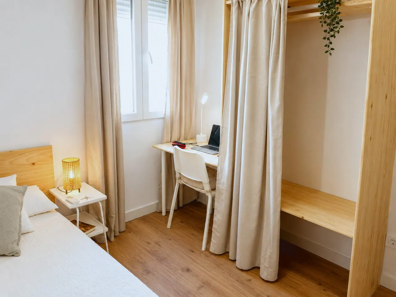 Habitación con cama individual, escritorio bajo la ventana y armario abierto de madera con cortina